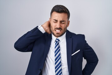 Handsome hispanic man wearing suit and tie suffering of neck ache injury, touching neck with hand, muscular pain
