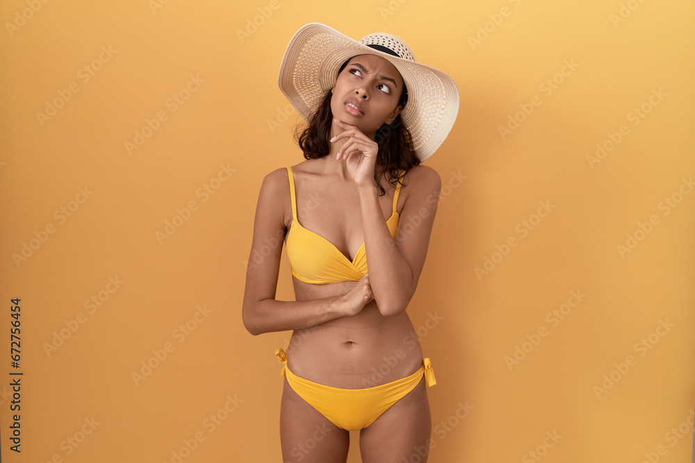 Poster Young hispanic woman wearing bikini and summer hat thinking worried about a question, concerned and nervous with hand on chin