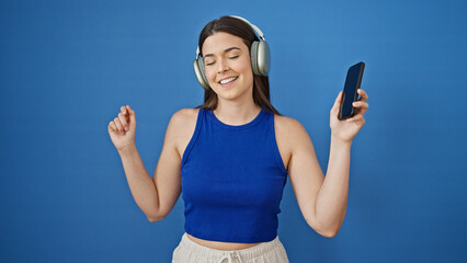 Young beautiful hispanic woman listening to music and dancing over isolated blue background