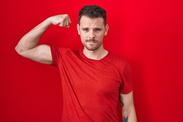 Fototapeta premium Young hispanic man standing over red background strong person showing arm muscle, confident and proud of power