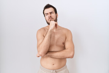 Fototapeta premium Young hispanic man standing shirtless over white background with hand on chin thinking about question, pensive expression. smiling with thoughtful face. doubt concept.