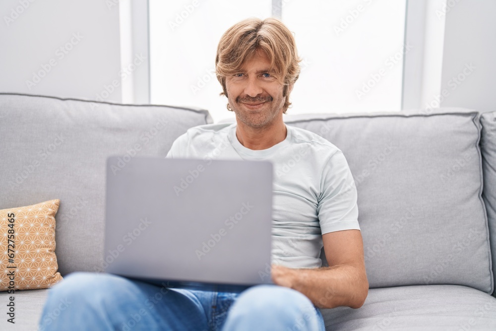 Poster Young man using laptop sitting on sofa at home