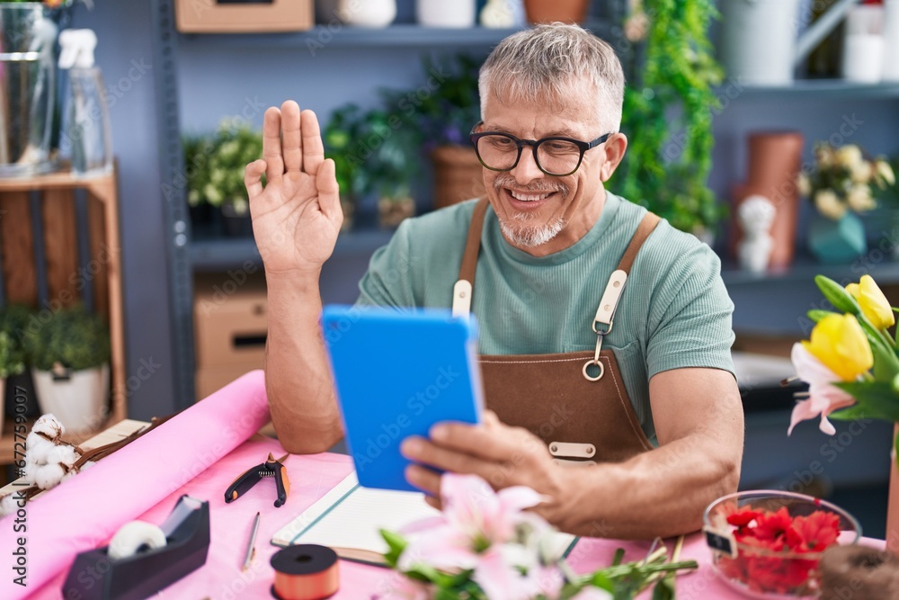 Wall mural Hispanic man with grey hair working at florist shop doing video call with tablet looking positive and happy standing and smiling with a confident smile showing teeth