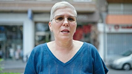 Middle age grey-haired woman standing with serious expression at street - obrazy, fototapety, plakaty