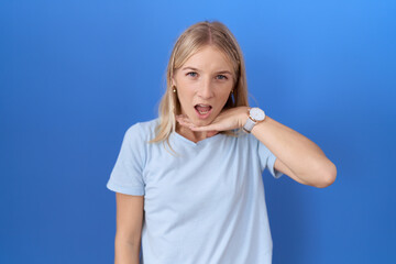 Young caucasian woman wearing casual blue t shirt cutting throat with hand as knife, threaten...