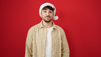 Young arab man wearing christmas hat with relaxed expression over isolated red background