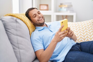 Young man using smartphone sitting on sofa at home