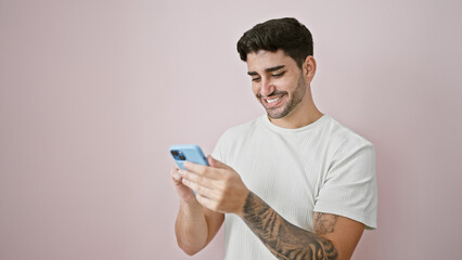 Young hispanic man using smartphone smiling over isolated pink background