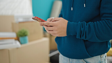 Young hispanic man using smartphone at new home