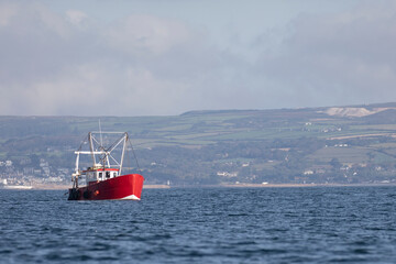 A bright red fishing trawler out to sea on the coast of Cornwall.