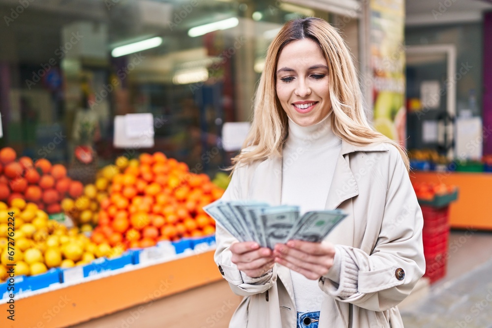 Poster young blonde woman smiling confident counting dollars at fruit store