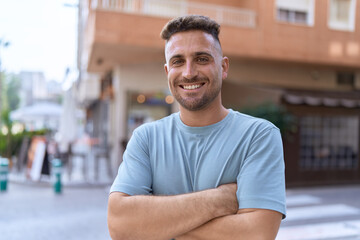 Young hispanic man standing with arms crossed gesture at coffee shop terrace
