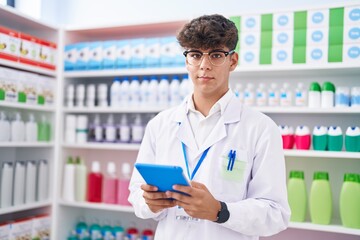 Young hispanic teenager pharmacist using touchpad working at pharmacy