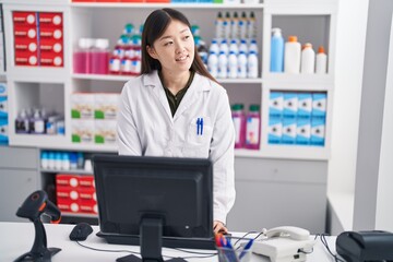 Chinese woman pharmacist smiling confident using computer at pharmacy