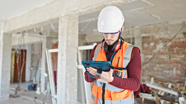 Young hispanic man builder using touchpad at construction site