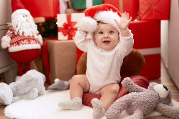 Adorable toddler smiling confident sitting on floor by christmas gift at home
