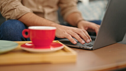 Young hispanic man typing on laptop at home