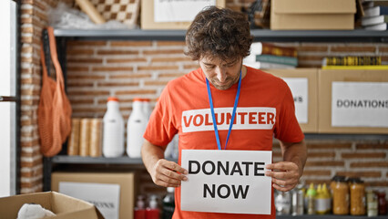 Young hispanic man volunteer holding donate now banner at charity center
