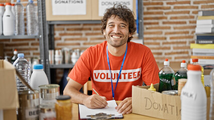 Young hispanic man volunteer writing on clipboard smiling at charity center