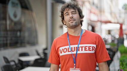 Young hispanic man activist wearing volunteer uniform standing with serious face at street