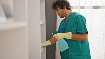 Young hispanic man cleaning shelving with a cloth at home