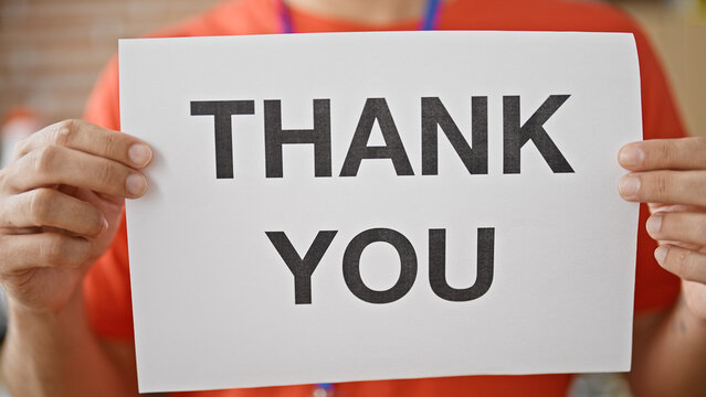 Young hispanic man volunteer holding thank you banner at charity center