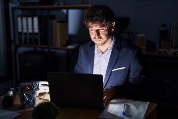 Hispanic young man working at the office at night puffing cheeks with funny face. mouth inflated with air, crazy expression.