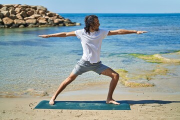 Young hispanic man doing yoga exercise standing at beach