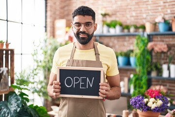 Hispanic man with beard working at florist holding open sign winking looking at the camera with...