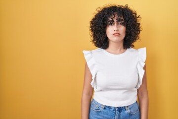 Young middle east woman standing over yellow background relaxed with serious expression on face. simple and natural looking at the camera.