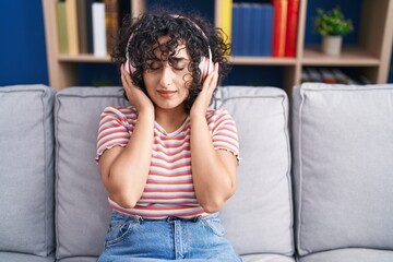 Fototapeta na wymiar Young middle eastern woman listening to music sitting on sofa at home