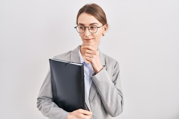 Young caucasian woman wearing business clothes and glasses looking confident at the camera smiling with crossed arms and hand raised on chin. thinking positive.