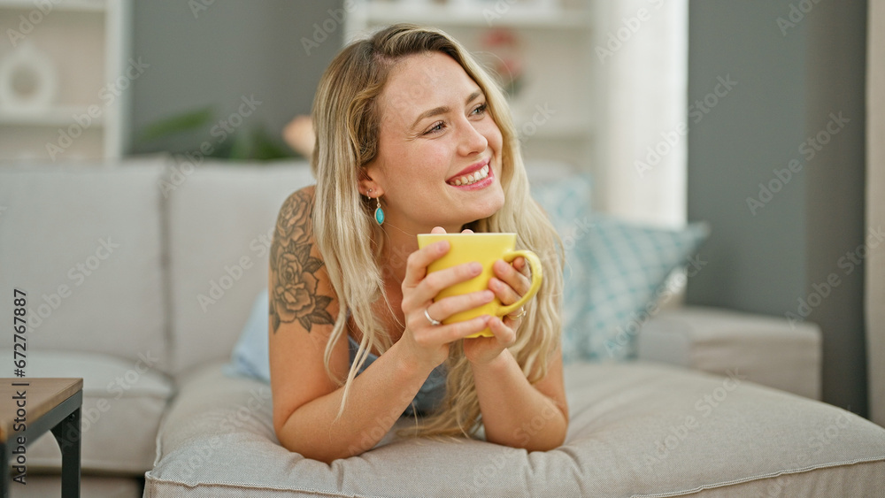 Sticker young blonde woman drinking coffee lying on sofa at home