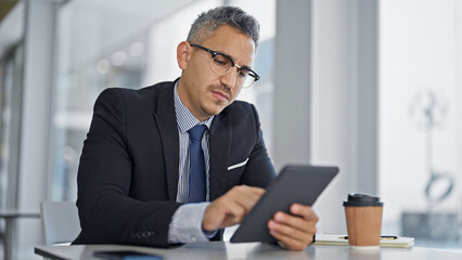 Young hispanic man business worker wearing glasses using touchpad at office