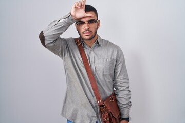 Young hispanic man wearing suitcase making fun of people with fingers on forehead doing loser gesture mocking and insulting.