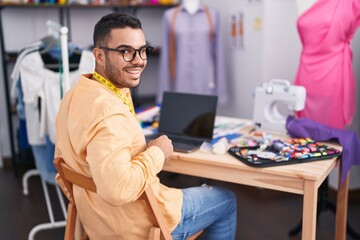 Fototapeta na wymiar Young hispanic man tailor smiling confident using laptop at tailor shop