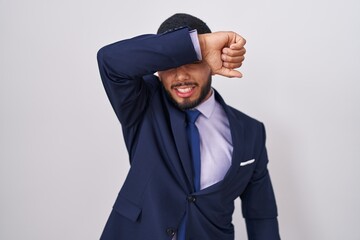 Young hispanic man wearing business suit and tie covering eyes with arm smiling cheerful and funny. blind concept.