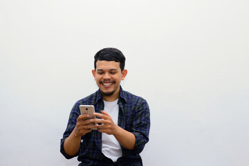 Adult Asian man clenched fist while holding smartphone and showing happy and enthusiastic expression