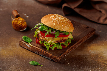 juicy cheeseburger with greens and tomatoes, on a wooden board, on a warm brown background, a saucer with mustard next to it, close-up