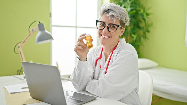 Young woman doctor holding pills bottle smiling at clinic