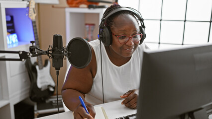Smiling african american woman, a confident musician, composing a soulful song in a music studio, engrossed in her musical world.