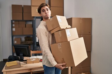 Young man working at small business ecommerce holding packages puffing cheeks with funny face. mouth inflated with air, catching air.