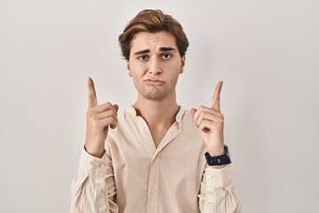 Young man standing over isolated background pointing up looking sad and upset, indicating direction...