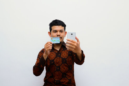 young adult man holds Indonesian identity cards (KTP) and smartphone. online finance debt concept.