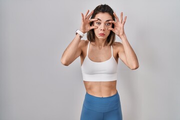 Hispanic woman wearing sportswear over isolated background trying to open eyes with fingers, sleepy...