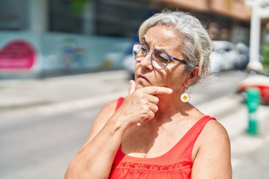 Middle age grey-haired woman standing with doubt expression at street
