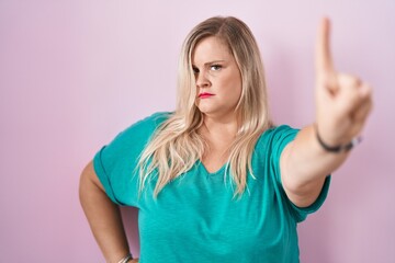 Fototapeta premium Caucasian plus size woman standing over pink background pointing with finger up and angry expression, showing no gesture