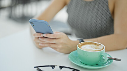 Young blonde woman using smartphone sitting on table at coffee shop terrace