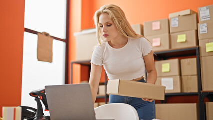 Young blonde woman ecommerce business worker using laptop holding package at office