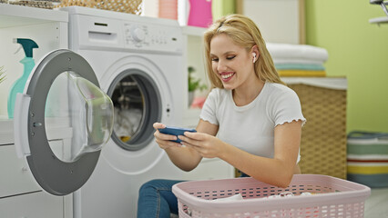 Young blonde woman playing video game washing clothes at laundry room